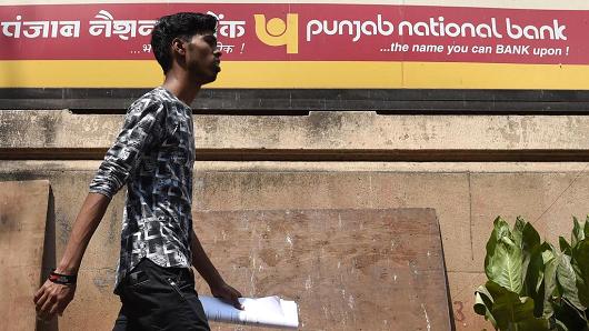 An Indian man walks past a sign for the state-owned Punjab National Bank (PNB) in Mumbai on February 14, 2018.